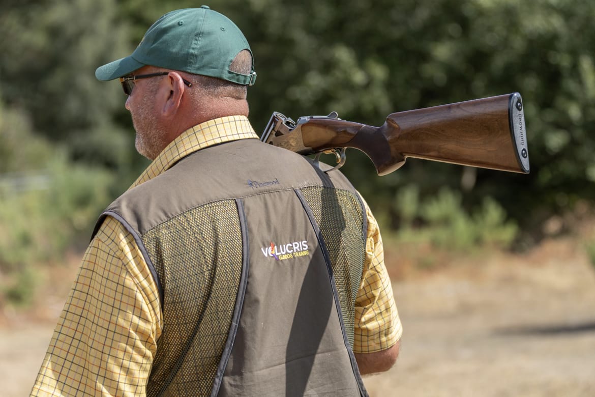 A handler in a Volucris Gundog Training vest carrying a shotgun over one shoulder.